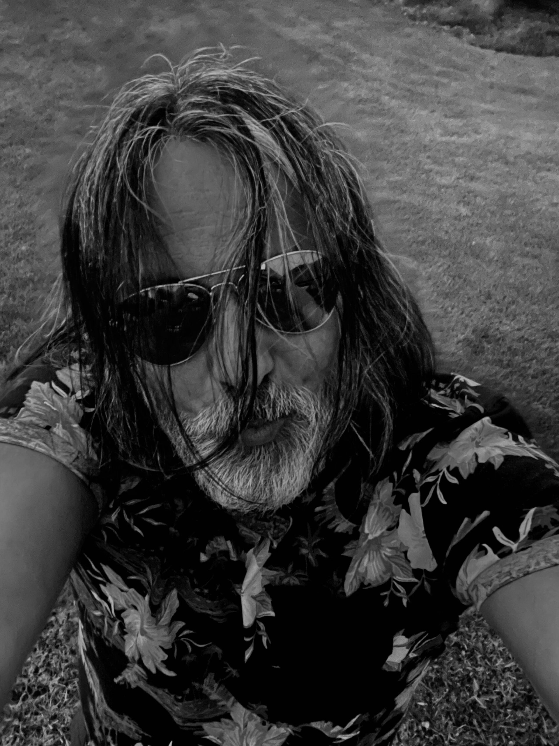 Selbstportrait bzw. Selfie von mir Nic Niggli selbst. Ich trage etwas längere Haare, eine Sonnenbrille, ein T-Shirt mit Blumenmuster. Das Foto ist in Schwarz-Weiß gehalten.